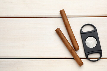 Cigars and guillotine cutter on white wooden table, flat lay. Space for text