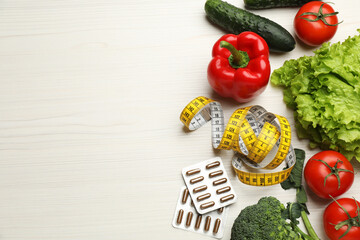 Weight loss pills, different vegetables and measuring tape on white wooden table, flat lay. Space for text
