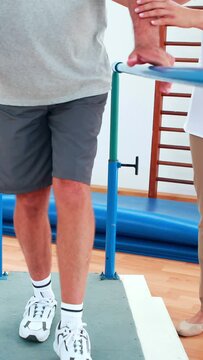 Physiotherapist helping patient walk with parallel bars