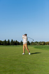 full length of senior man in flat cap playing golf on green lawn.
