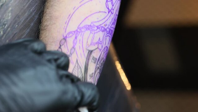 Close up of a young professional tattoo master introduces black ink into the skin using needle from a wireless tattoo machine. Tattoo on hand. Vertical video
