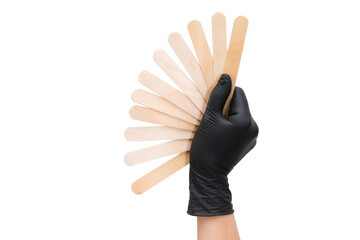 hand in a black glove holds wooden sticks for depilation on white isolated background