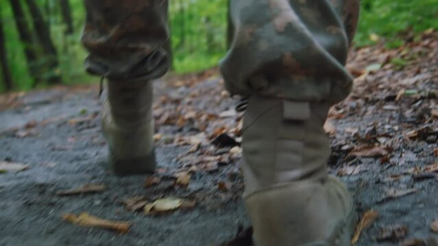 Close up soldier male legs in army boots walk falls to the ground wounded in camouflage uniform. In forest