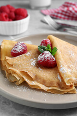 Delicious crepes served with mint, raspberries and powdered sugar on grey table, closeup