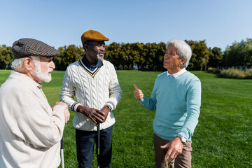 senior asian man gesturing and talking with multiethnic friends on golf field.