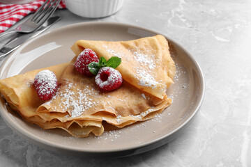 Delicious crepes served with mint, raspberries and powdered sugar on grey table, closeup