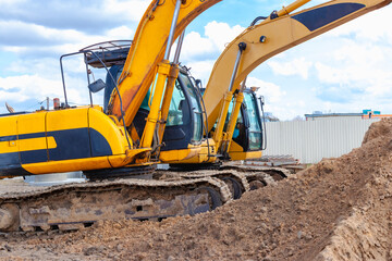 Two powerful excavators work at the same time on a construction site, sunny blue sky in the background. Construction equipment for earthworks.