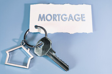 The concept of mortgage, sale and rental of housing and real estate. Mortgage credit lending. Keychain in the shape of a house with a key on a blue background.