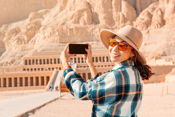 Travel blogger girl takes pictures on a smartphone at the famous Hatshepsut temple in the ancient...