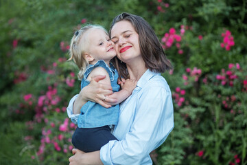 Mom holds toddler daughter in her arms. Gentle hugs of mom. Rest in the park in the spring.