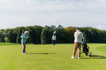 Obraz premium senior asian man playing golf near interracial friends with flag stick and golf cart.