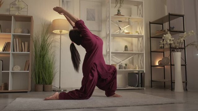 Yoga practicing. Home training. Sporty lifestyle. Flexible peaceful stretching woman training anjaneyasana pose low lunge exercise at living room.