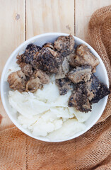Mogodu, a Traditional South African stew made of chopped innards of a cow or tripe served with pap or maize meal. flat lay on light wood with burlap cloth and copy space