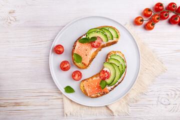Fototapeta na wymiar Healthy avocado toasts with rye bread with salted salmon, cream cheese, fresh tomatoes, sesame seeds, basil on plate. Homemade sandwiches for breakfast or lunch. Seafood. Top view. 