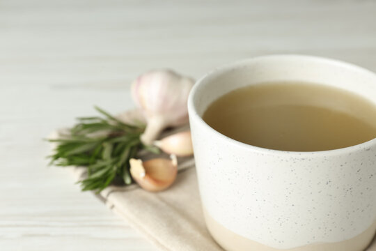 Mug with delicious bone broth on white wooden table, closeup. Space for text