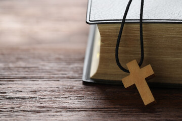 Wooden Christian cross and Bible on table, closeup. Space for text