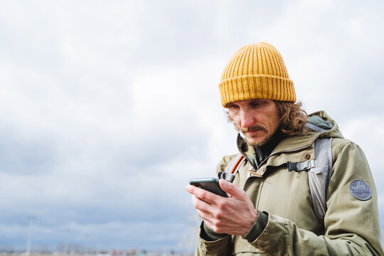 A hipster in a yellow hat holds a phone in his hands, a man types text on a smartphone, call a friend, a traveler looks at a map on a navigator.