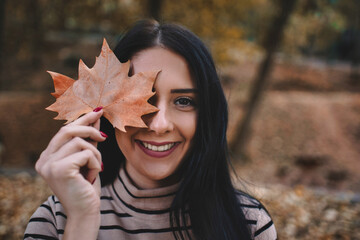 Autumn outdoor portrait of cute smiley women holding autumn leaves near the face.