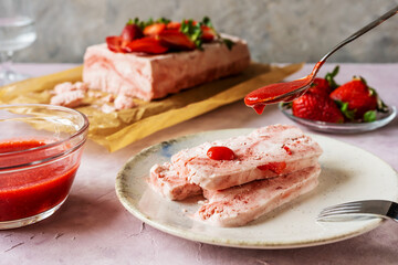 Italian strawberry dessert Semifreddo on plate with teaspoon pouring strawberry's sauce
