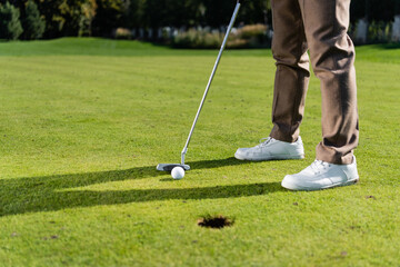 Plakat cropped view of man in white sneakers playing golf on lawn.