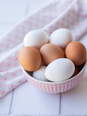 Close up view of raw white and brown eggs in pink plate on white background with towel. Healhty food concept. Image for homemade receipe, morning routine, kitchen interior.