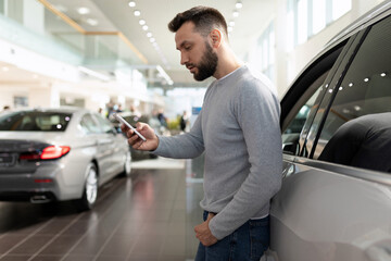 a man on the phone studies the features of an SUV in a car dealership