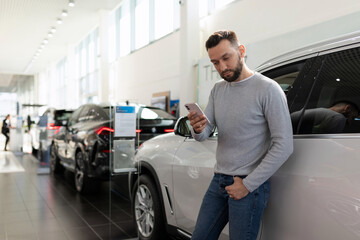 Fototapeta na wymiar a man studies the offer of insurance companies in a car dealership on a smartphone