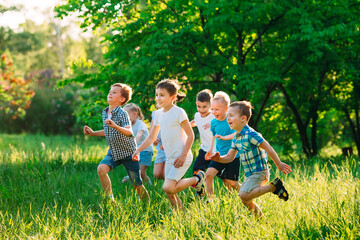 A group of happy children of boys and girls run in the Park on the grass on a Sunny summer day.