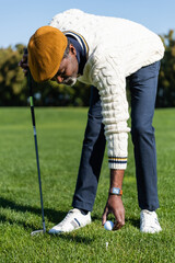 bearded african american man placing ball on golf tee.