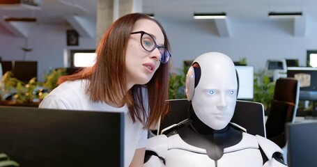 Close up of robot and woman cooperating. Woman talking, helping. Android working at computer in coworking space with female. Humanoid as IT worker. Futuristic communication. Artificial intelligence