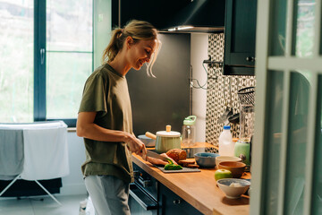 A young happy blond smiling woman cooking food in a home kitchen..