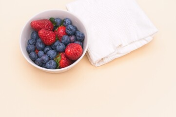 mixed fresh organic berries in a bowl with white napkin on a beige table