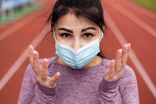 Woman dressed sports suit wear face blue disposable mask. Female athlete at the stadium treadmill, new mutating strain coronavirus illness prevention outbreak pandemic health risk concept
