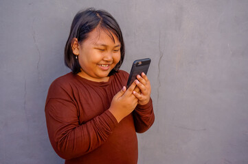 Fototapeta premium Portrait of young fun smart happy little asian girl holding smart phone isolated on wall background. Education for elementary kindergarten.