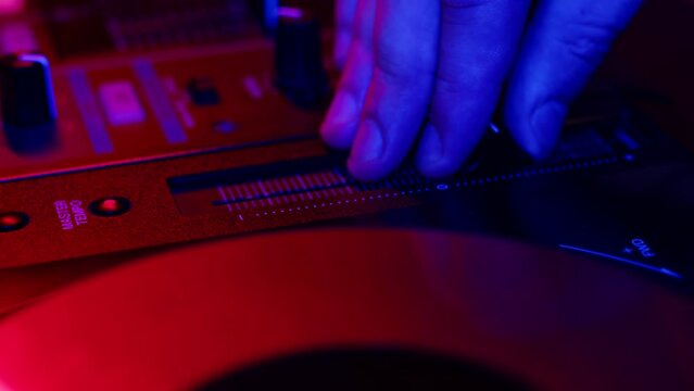 DJ hand lowers fader down to turn down volume of music in nightclub at disco, closeup. DJ presses buttons and slider on mixer in club at party