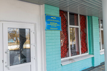  War of Russia against Ukraine. Concept of invasion. Village school with broken windows after bomb explosion. It is written on plate "Bilozirka secondary school"