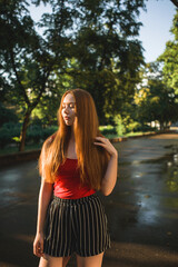 Young beautiful red-haired long-haired woman in a summer pink dress walks through the streets of a summer city.