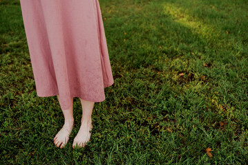 A girl in a pink dress stands barefoot on the grass.