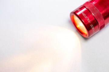 Metal flashlight in close-up fire red color with selective focus on isolated white background. Made in USA California, the flashlight illuminates the ground in low light with its yellow light.