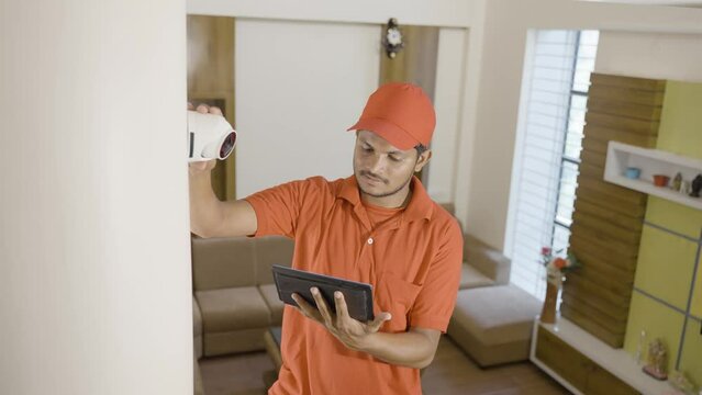 electrician fixing cctv camera while checking angle or settings in digital tablet at home - concept of technology, professional worker and safety.