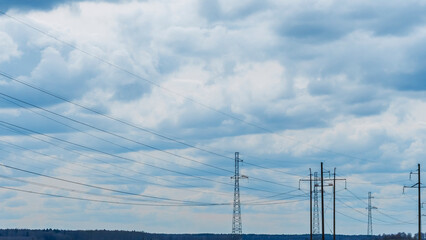 High voltage post on blue sky with clouds background. Electrical net of poles on blue sky and spring meadow.