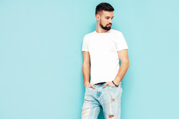 Portrait of handsome confident stylish hipster lambersexual model.Man dressed in white T-shirt and jeans. Fashion male isolated on blue wall in studio