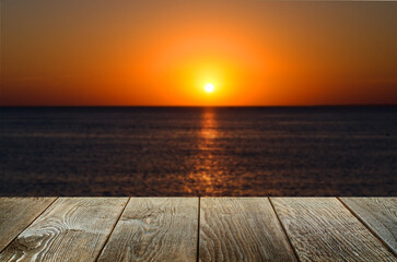 An empty brown wooden table. Blurred background with sunset on the sea.