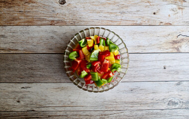 Top Views of Fresh red, green and yellow bell peppers (capsicum) are cut into small pieces. in a clear glass bowl laying on the wooden floor background. Concept for health and vitamins.