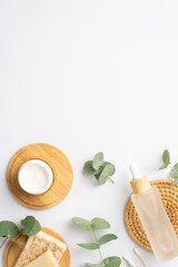 Top view vertical photo of transparent bottle with liquid cotton buds cream bottle soap on wooden stand and eucalyptus on isolated white background with empty space