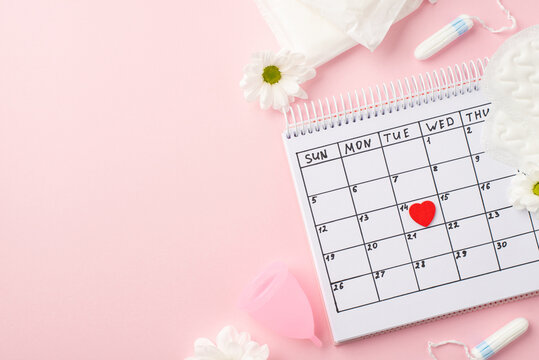 Top view photo of red heart mark on the calendar camomile flower buds menstrual cup hygienic pads and tampons on isolated pastel pink background with empty space