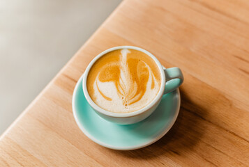 Cappuccino with beautiful latte art in a blue ceramic mug. Coffee for breakfast in the coffee shop. A mug of latte on a flatlay wooden table