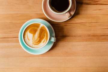 Cappuccino and Americano on a wooden table view from above. Creative coffee concept with space for text. Fragrant cappuccino in a blue mug and black Americano in a pink cup flatlay