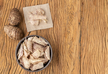 Yam or taro chips in a bowl with raw vegetable over wooden table with copy space