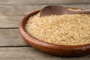 Narrow focus, raw brown rice in a plate over wooden table with copy space